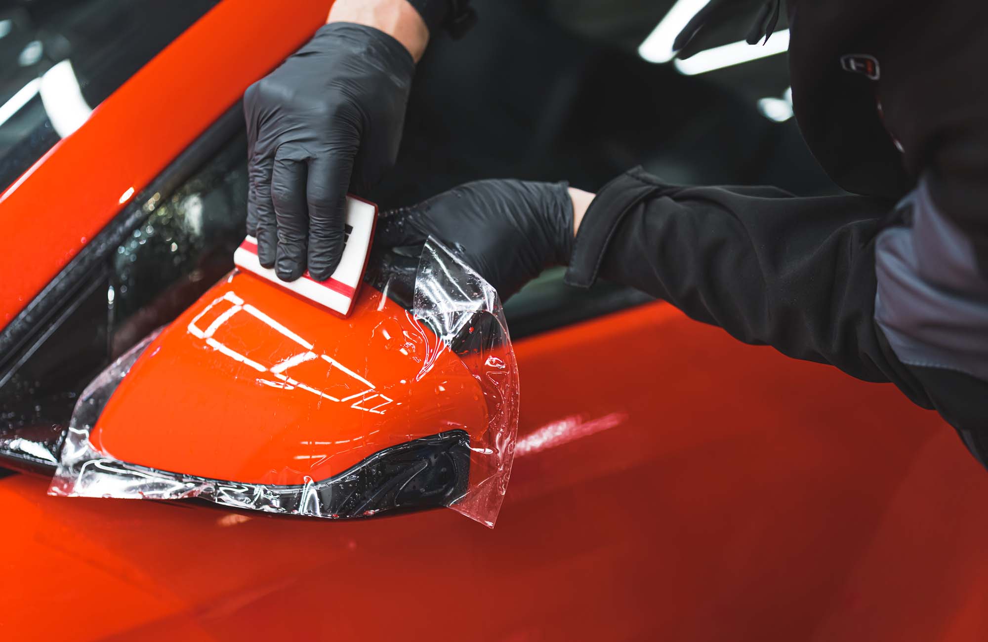 The process of installing PPF on the side mirror of a red sports car. Protective film for paint protecting scratches and gravel. High quality photo